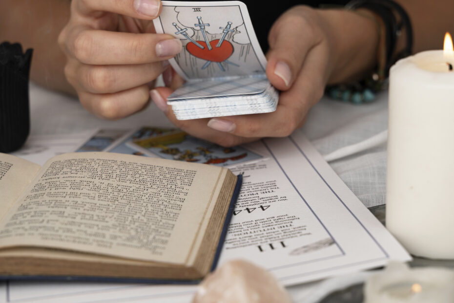 Pessoa segura carta de tarô Três de Espadas com livro aberto e vela acesa, simbolizando o tarô como ferramenta filosófica.